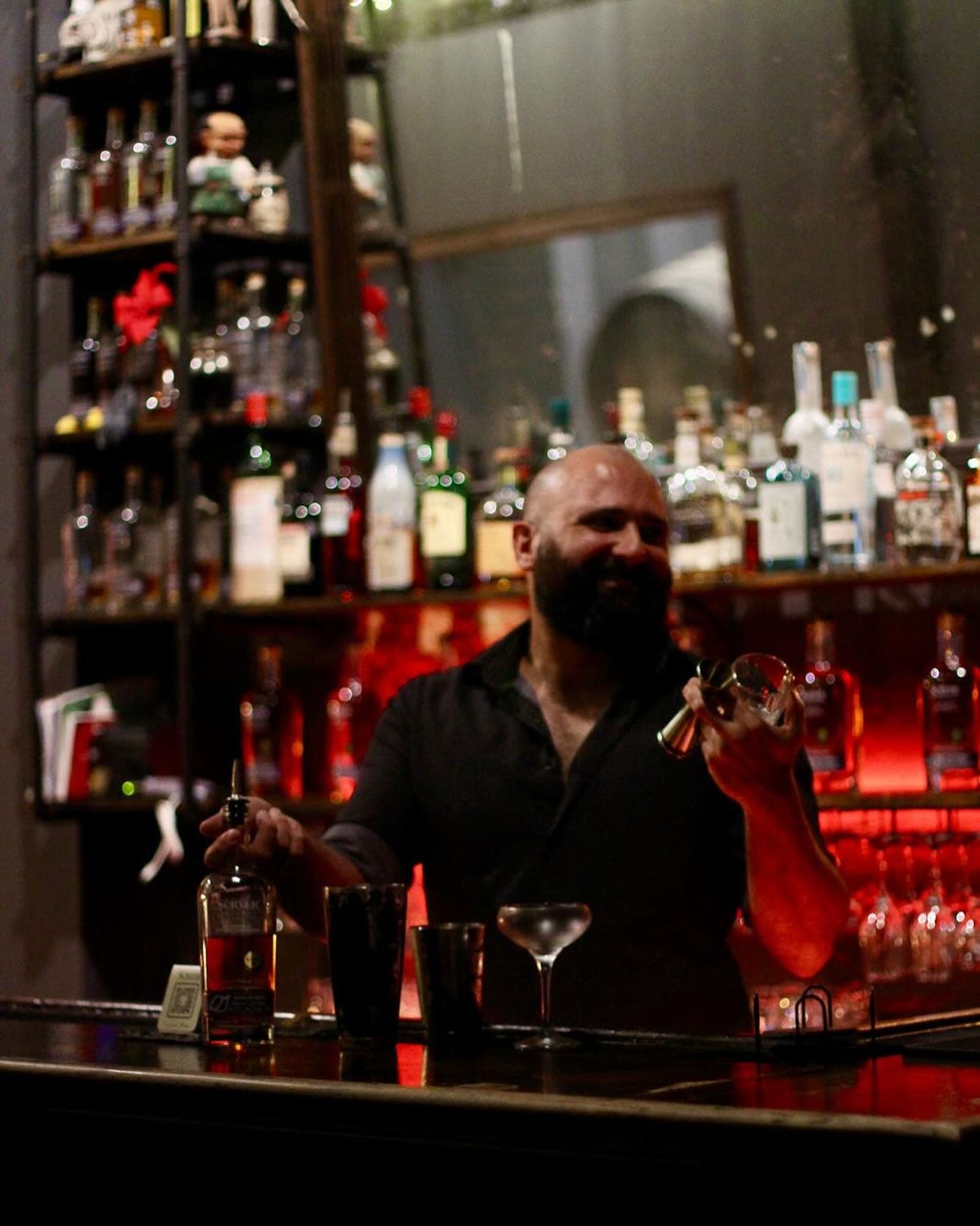 Iván Avilés smiling behind a bar while preparing a cocktail